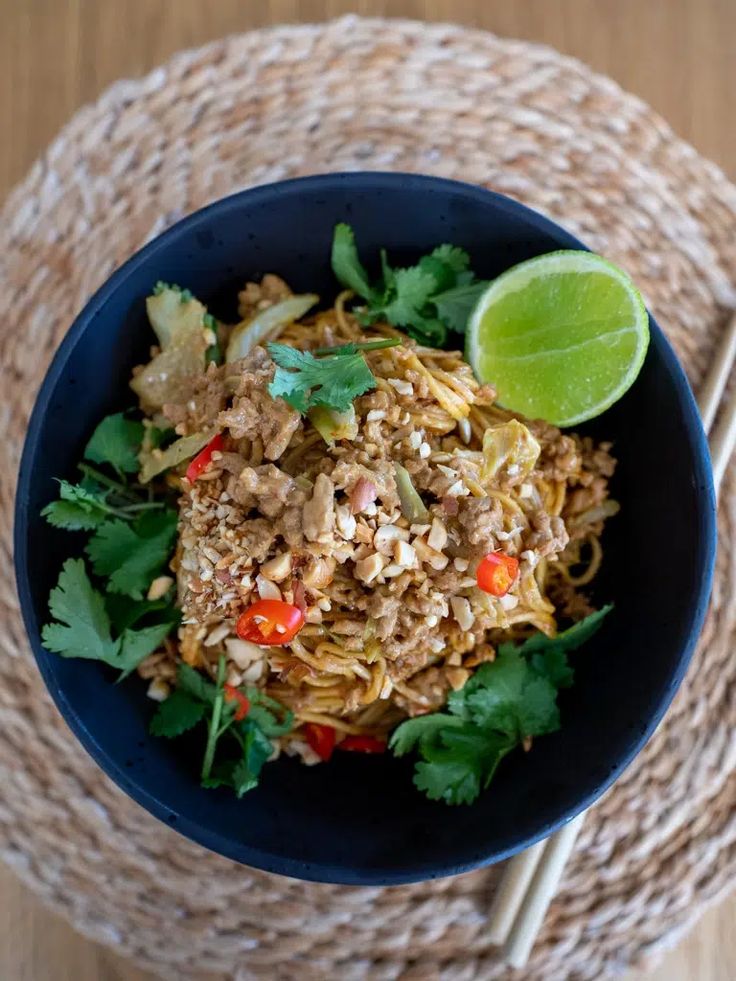 a blue bowl filled with noodles, meat and veggies next to chopsticks