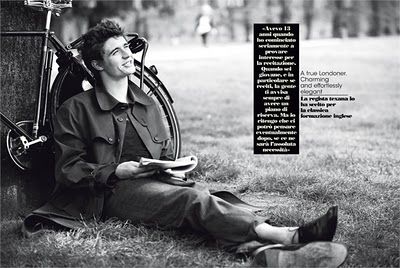 a man sitting on the ground next to a bike and holding a book in his hands