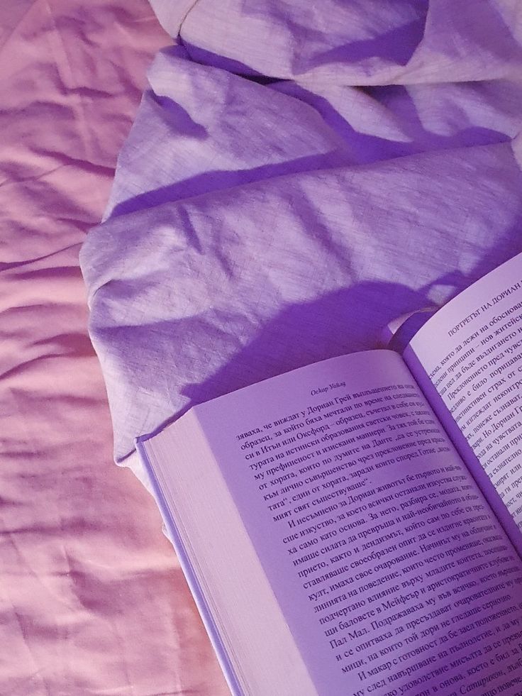 an open book sitting on top of a bed next to a pink comforter and pillows