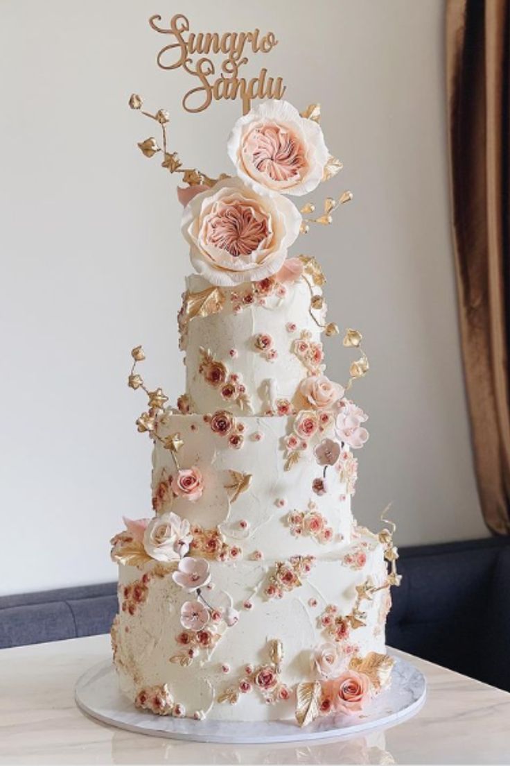 a three tiered wedding cake with pink flowers on the top and gold lettering that says sugarboar sandy