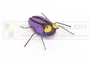 a purple bug with yellow eyes sitting on top of a white surface