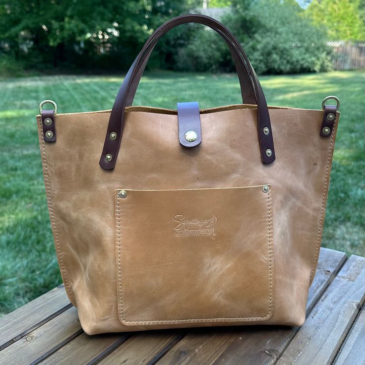 a brown and tan bag sitting on top of a wooden table next to a green field