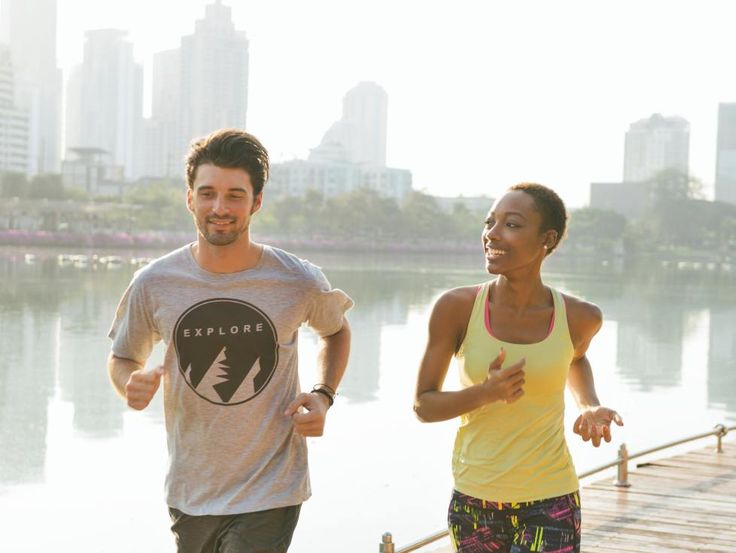 a man and woman running on a boardwalk near the water