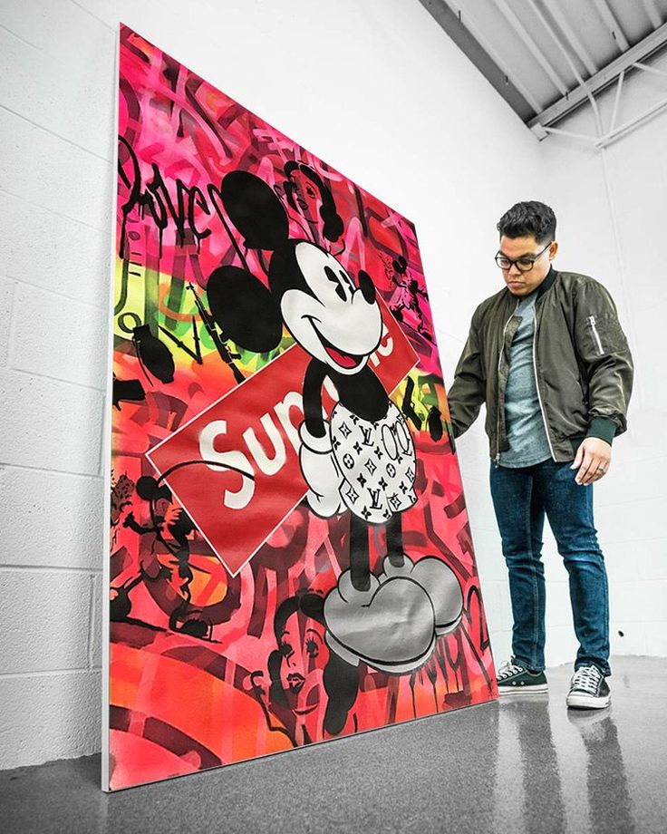 a man standing in front of a large mickey mouse sign with graffiti on it's side