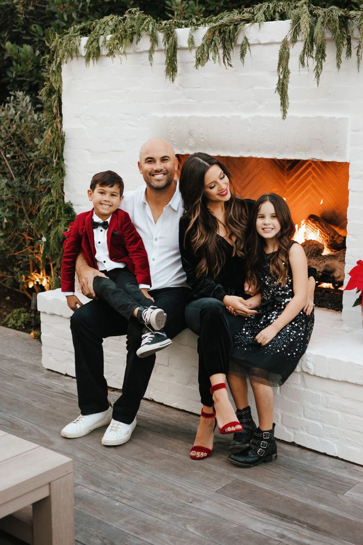 a family sitting on a bench in front of a fireplace with christmas decorations around it