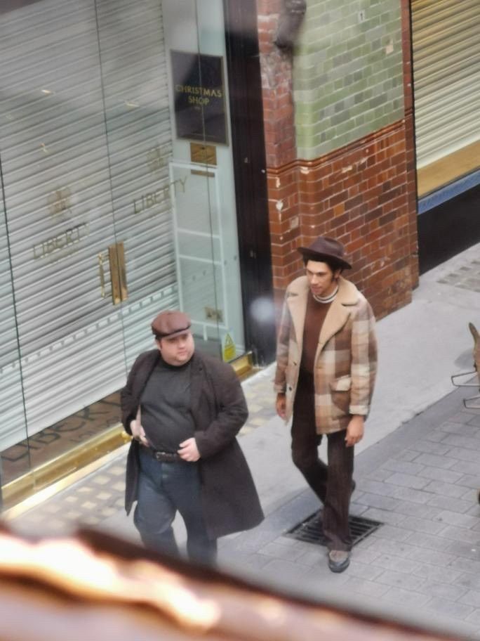 two people walking down the sidewalk in front of a store