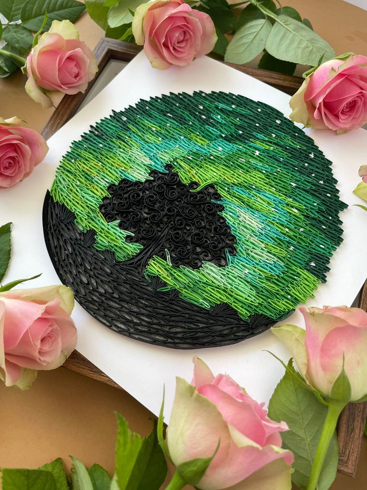 there is a green and black paper on the table with roses around it that have been made to look like a tree