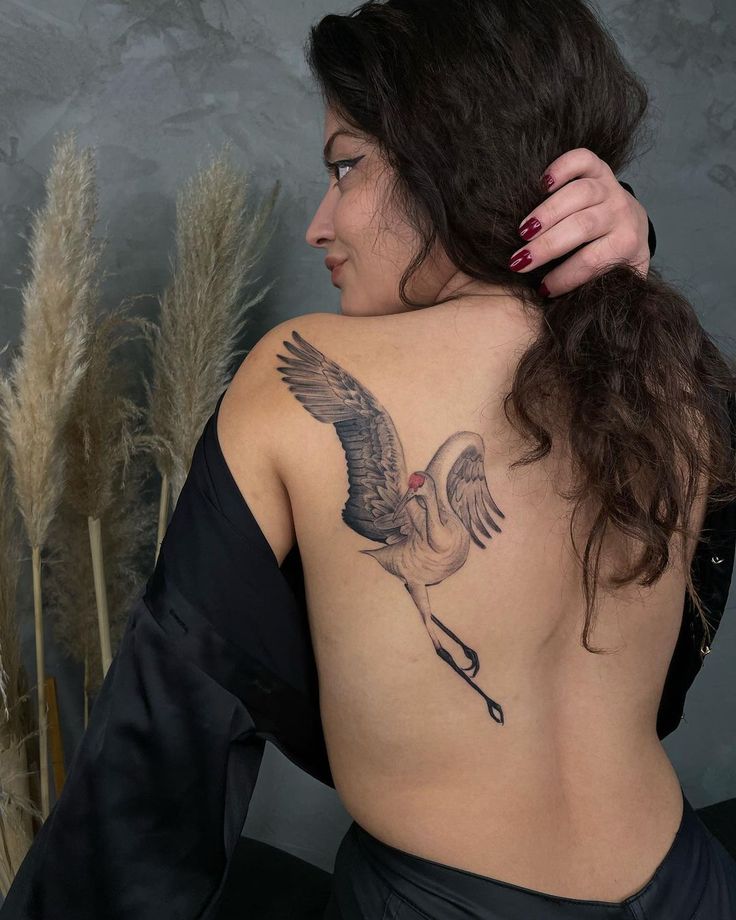 the back of a woman's body with a crane tattoo on her upper back