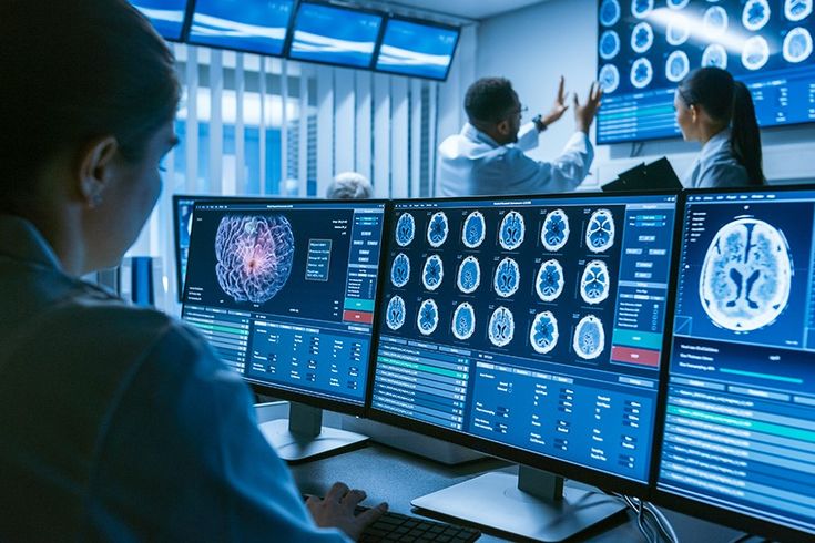 a woman sitting in front of two computer monitors with brain images on the monitor screen