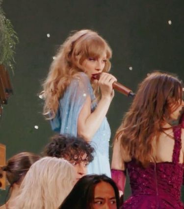 two women in dresses are singing into microphones while others watch from the sidelines