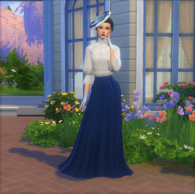 a woman in a long blue dress is standing by a house with flowers and plants