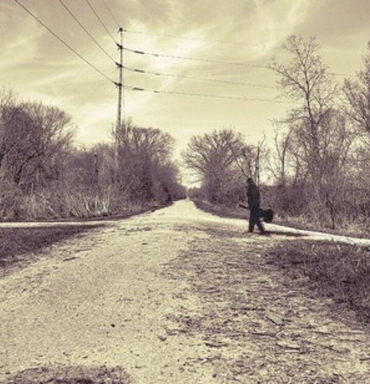 a person walking down a dirt road with power lines above them and trees in the background