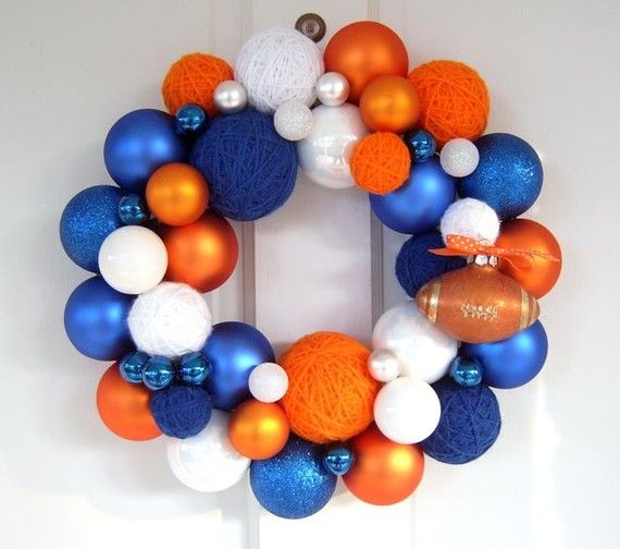 an orange, white and blue wreath is hanging on the front door with ornaments around it