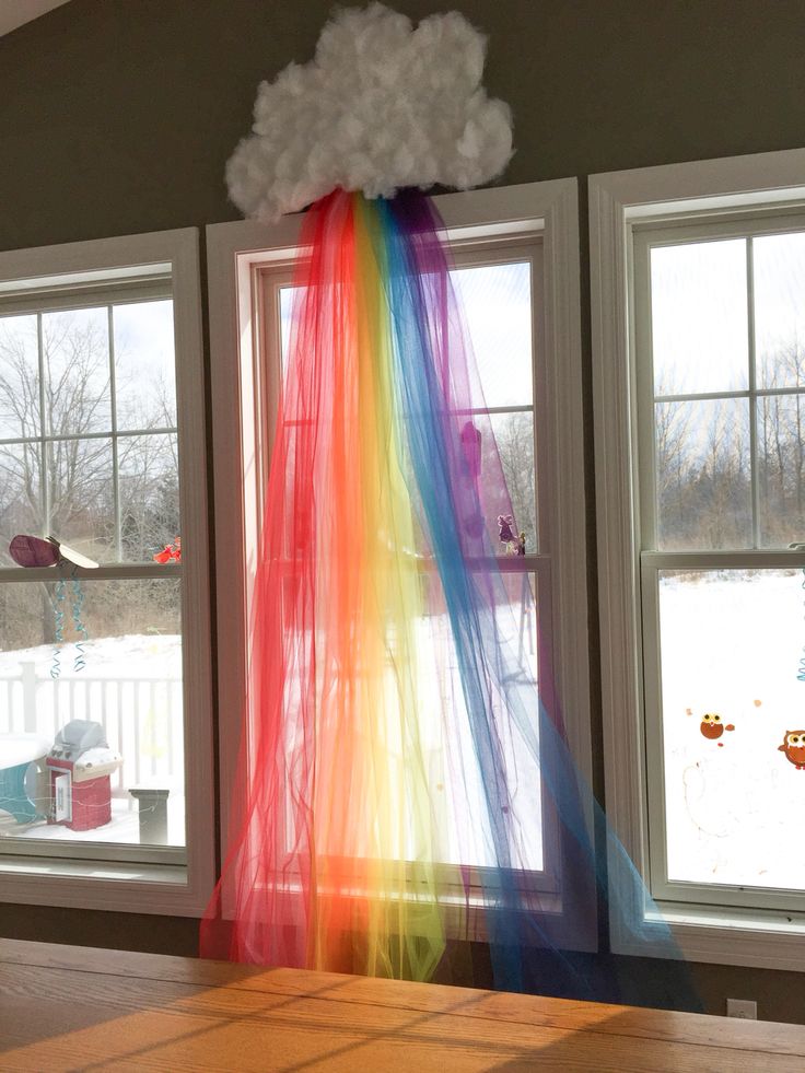 there is a rainbow curtain in the middle of a room with two windows and a cloud hanging from the ceiling