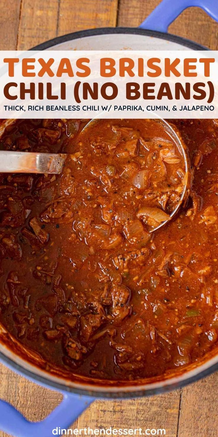 a blue pot filled with chili and beans on top of a wooden table next to a spoon