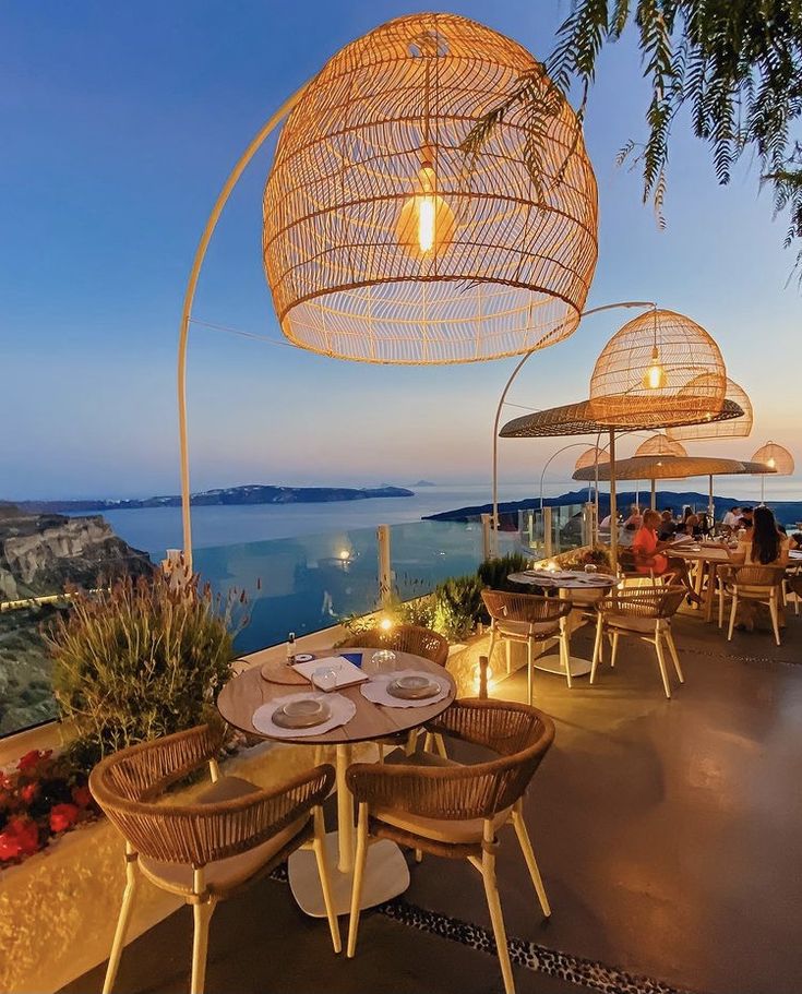 an outdoor dining area with wicker chairs and umbrellas overlooking the ocean at dusk