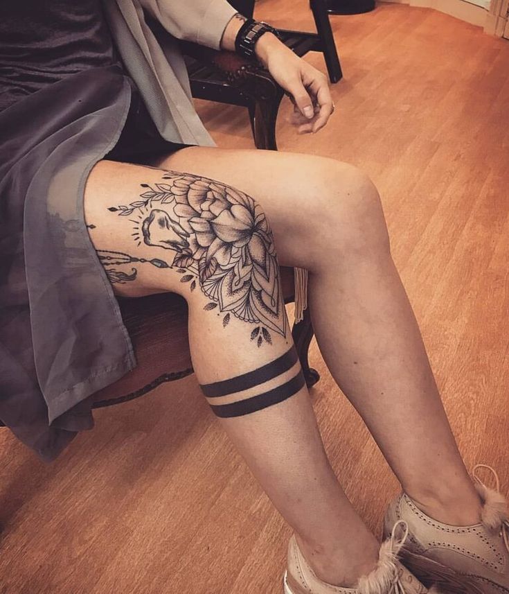 a woman sitting on top of a wooden floor next to a chair with tattoos on her legs