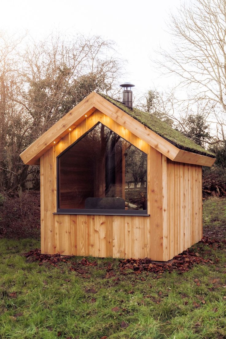 a small wooden building with a green roof and lights on it's windows in the grass