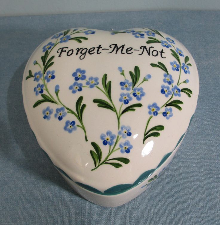 a ceramic heart shaped box with forget me not written on the side and blue flowers painted on it