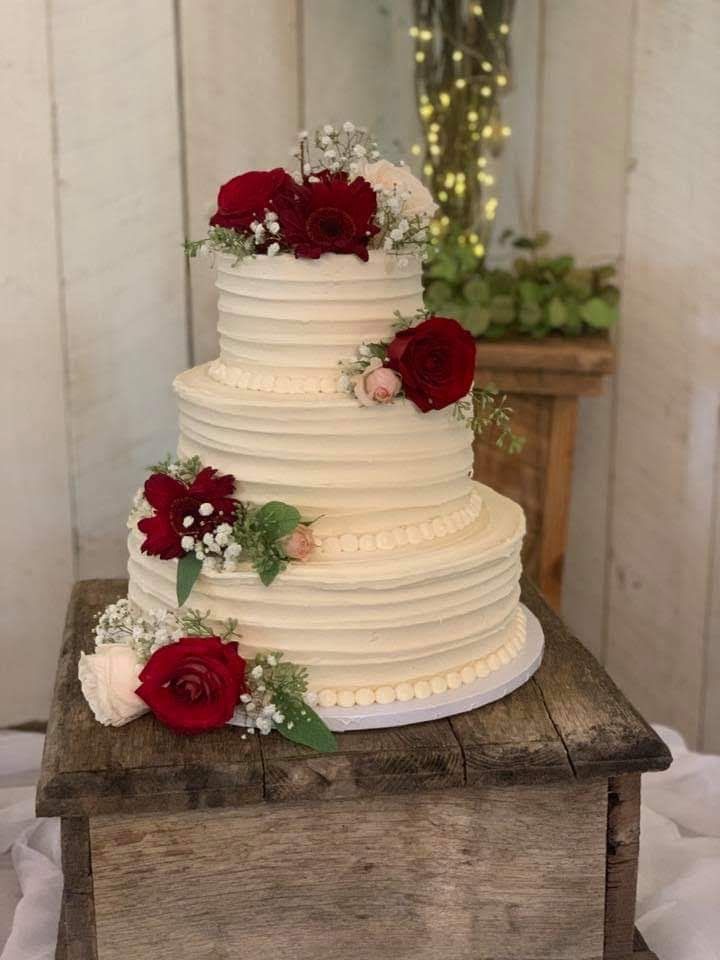 a three tiered wedding cake with red and white flowers on the top is sitting on a wooden box