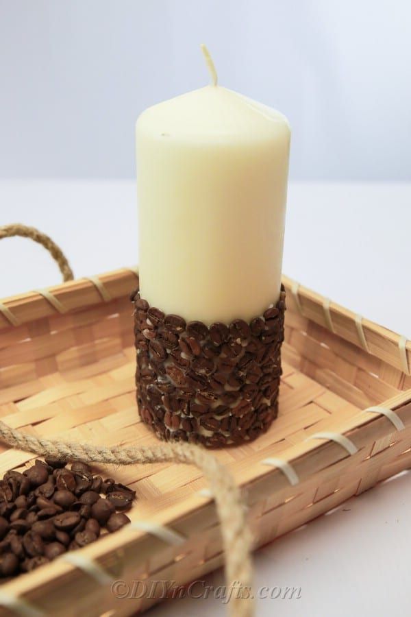 a white candle sitting on top of a wooden tray with coffee beans in front of it