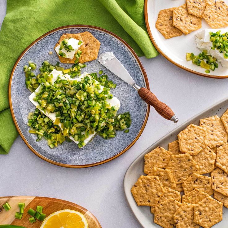 an assortment of crackers and vegetables on plates with green napkins next to them