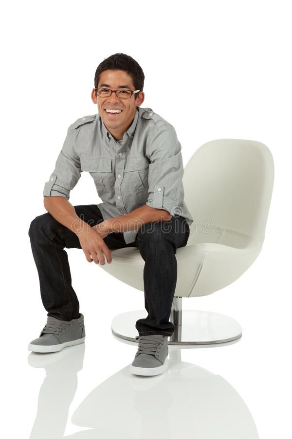 a man sitting on a white chair with his legs crossed and smiling at the camera