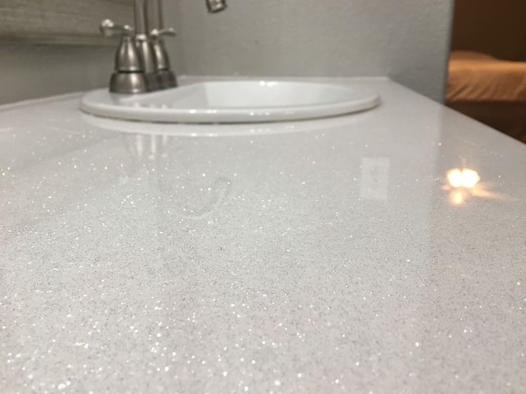 a white counter top in a bathroom with a sink and faucet next to it