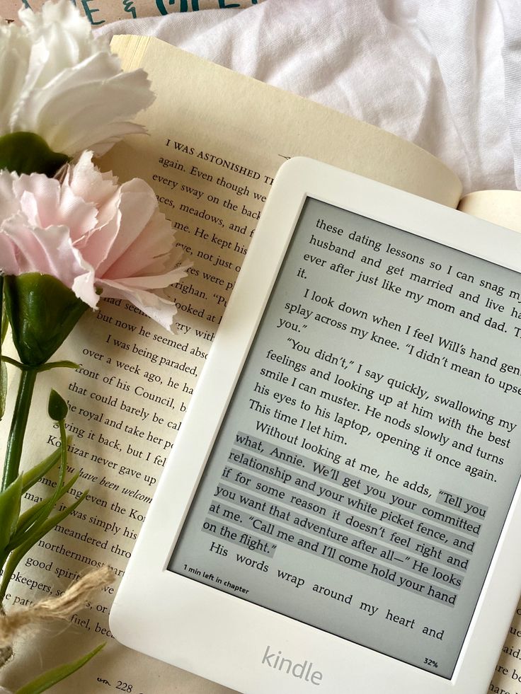 an open book sitting on top of a table next to flowers and a vase with pink carnations