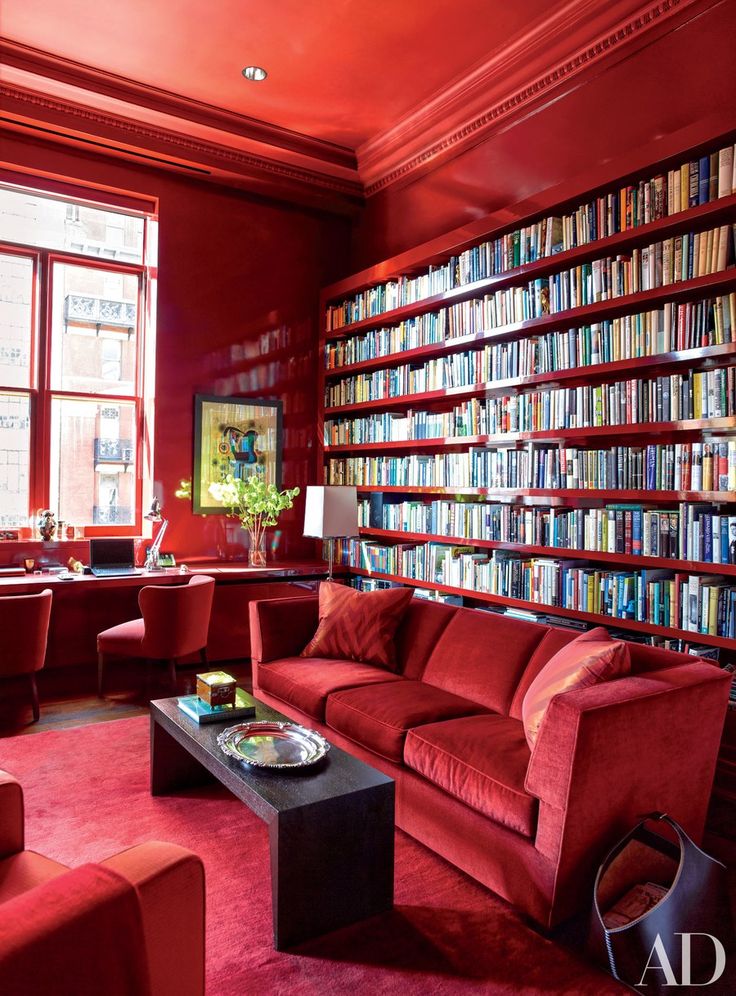 a living room filled with lots of red furniture and bookshelves full of books