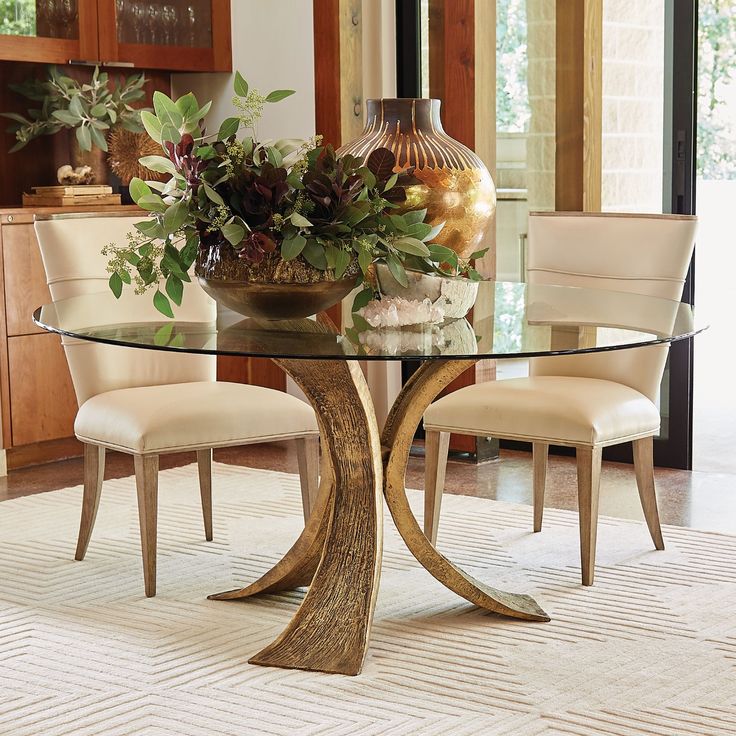 a glass table topped with a vase filled with flowers next to two chairs and a rug