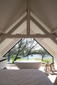 a large white bathtub sitting under a window in a bedroom next to a wooden stool