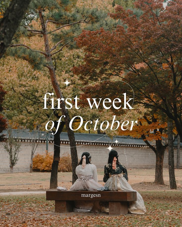 two women sitting on a bench in the middle of a park with trees and leaves