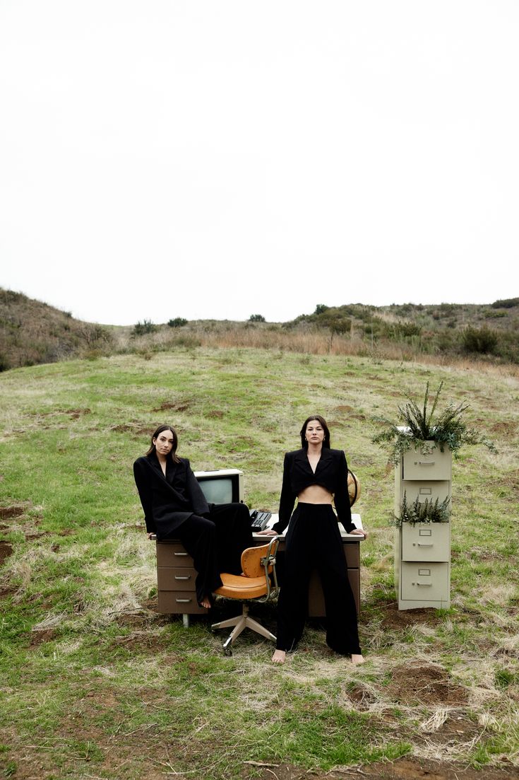 two women sitting in chairs on top of a grass covered hill