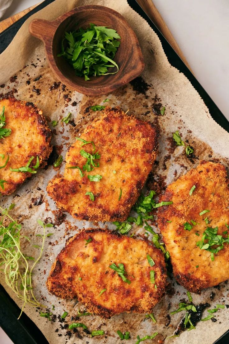 four pieces of breaded chicken sitting on top of a pan next to a bowl