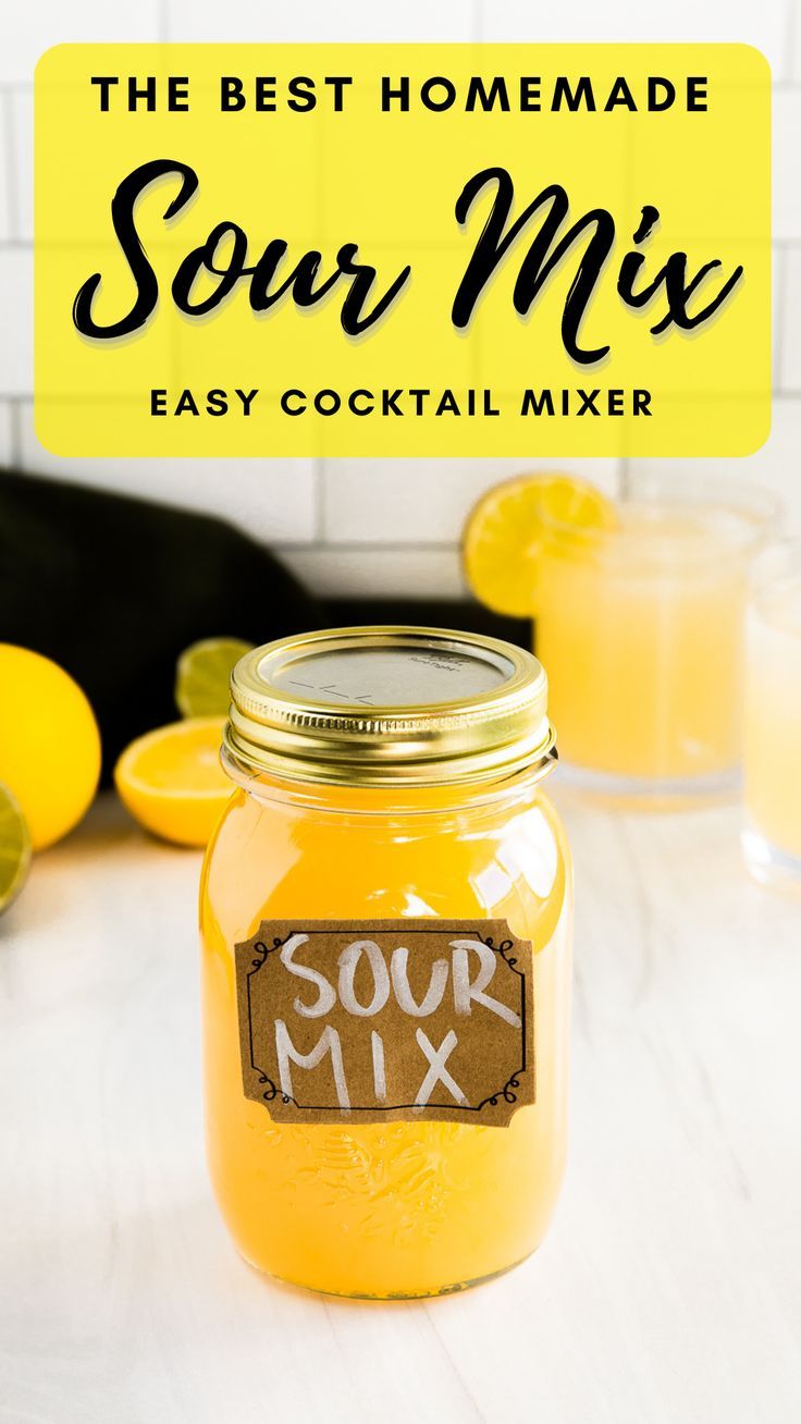 a mason jar filled with sour mix sitting on top of a table next to lemons