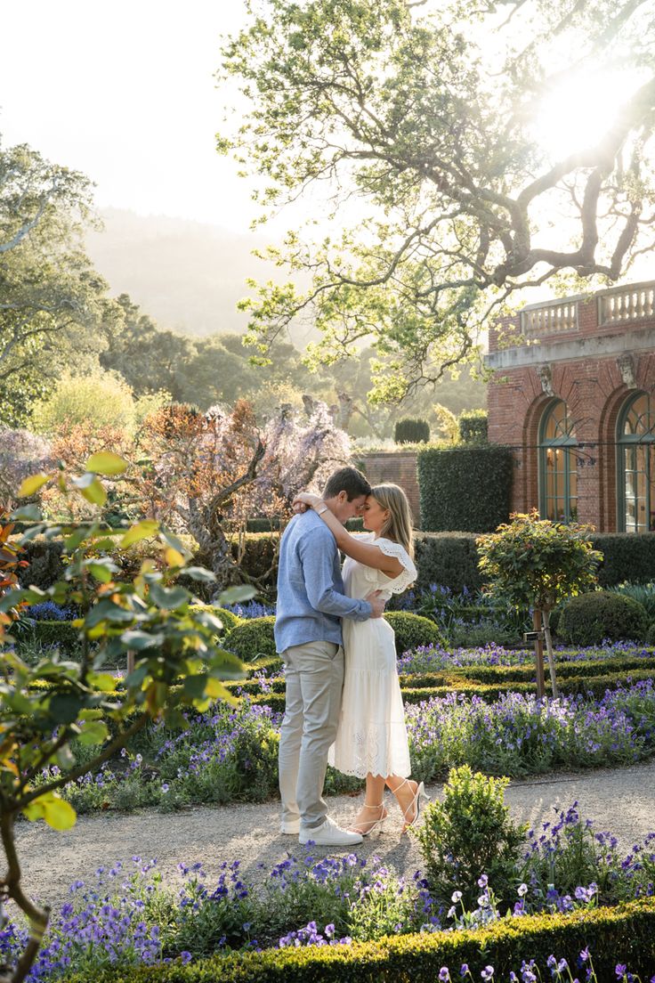 a man and woman embracing in the middle of a garden with purple flowers around them