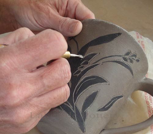 a person is drawing on a vase with a white pencil and some sort of brush