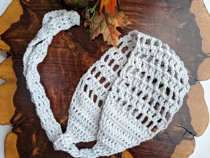 a white crocheted bag sitting on top of a wooden table next to an autumn leaf