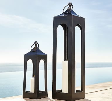 two black lanterns sitting next to each other on a table near the water and sky