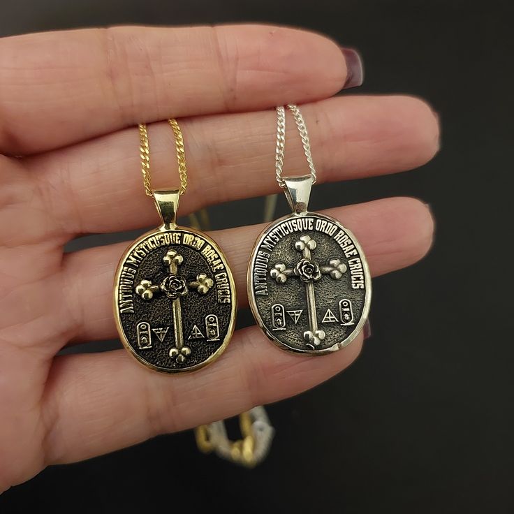 two pendants that have been placed on someone's hand, one is gold and the other is silver