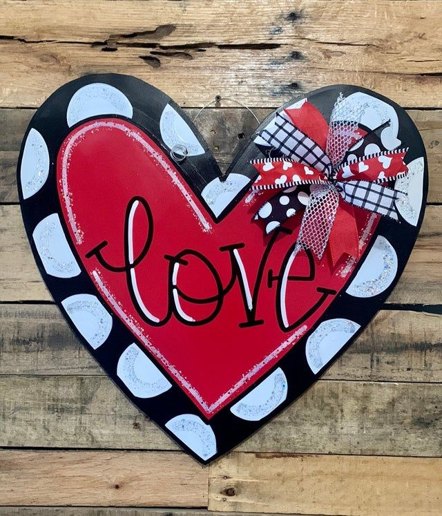 a heart shaped sign with the word love painted on it and a bow tied to it