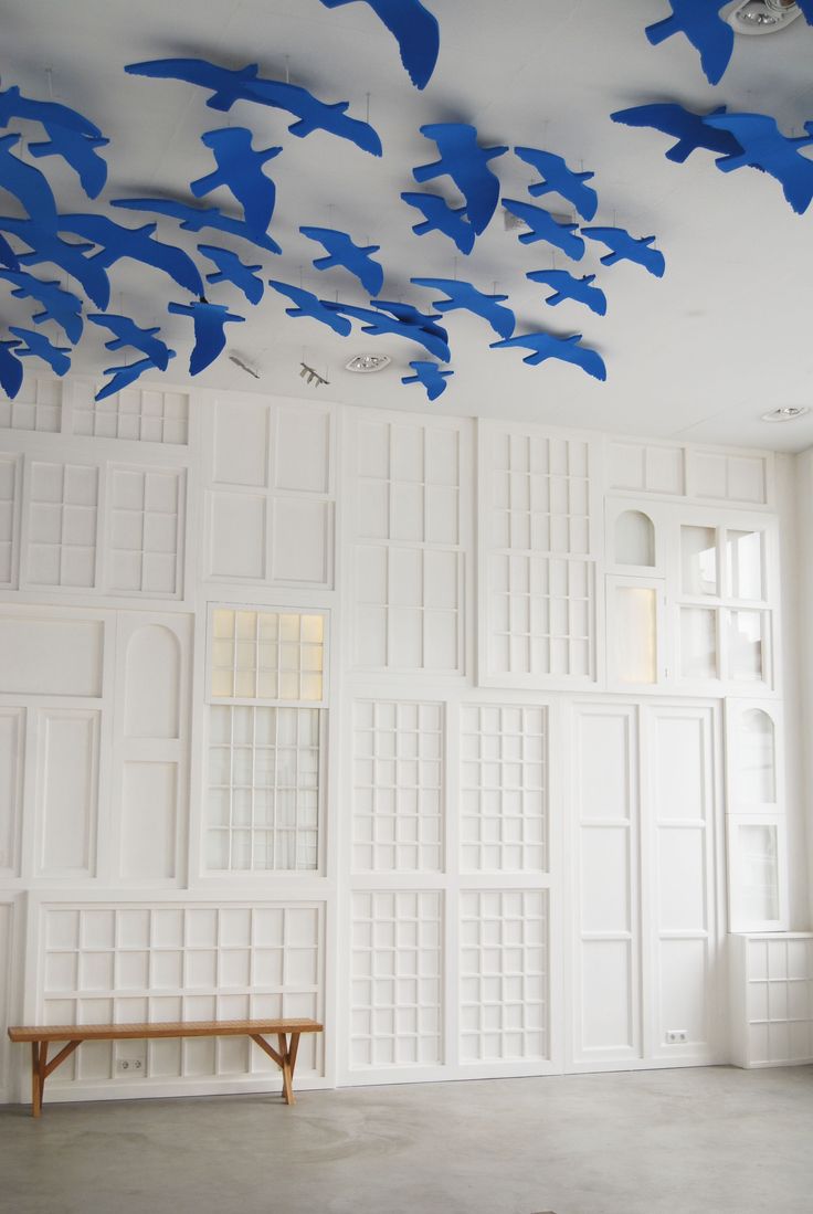 blue birds are flying in the air above a white room with large windows and wooden benches