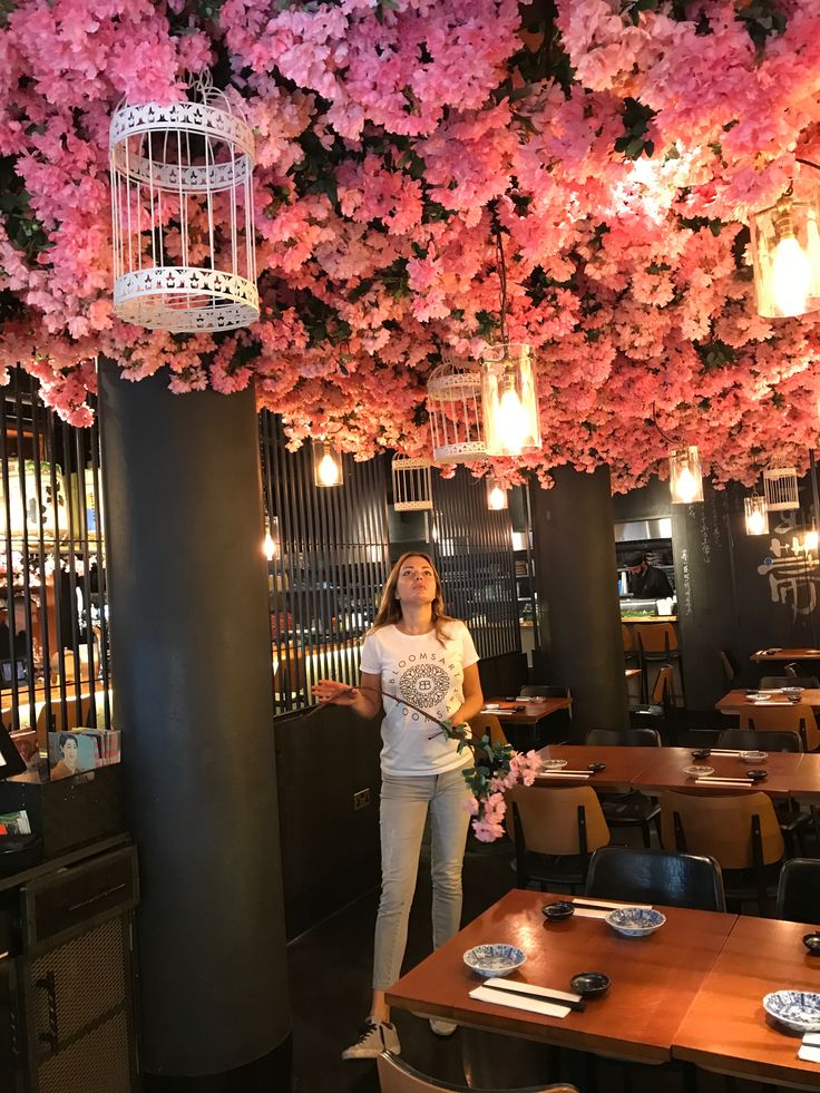 a woman standing in front of a table with flowers on it and a birdcage hanging from the ceiling