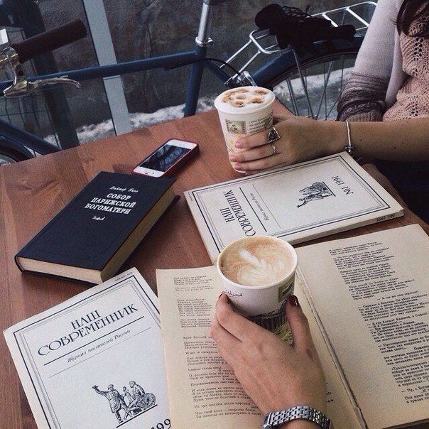 two people sitting at a table with coffee and books