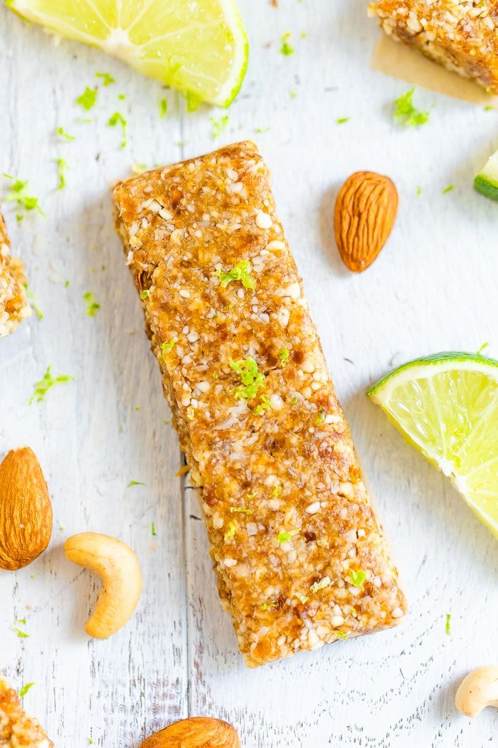 almond, lime and pistachio granola bars on a white table with nuts