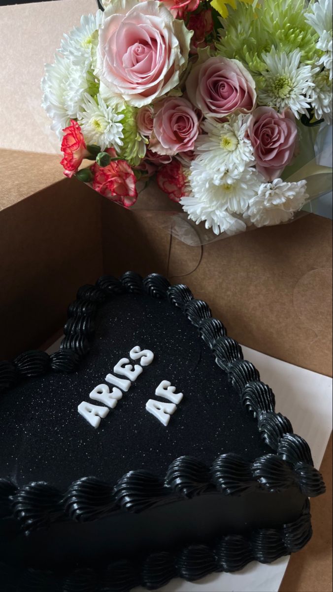 a black heart shaped cake with the word apricos on it next to flowers