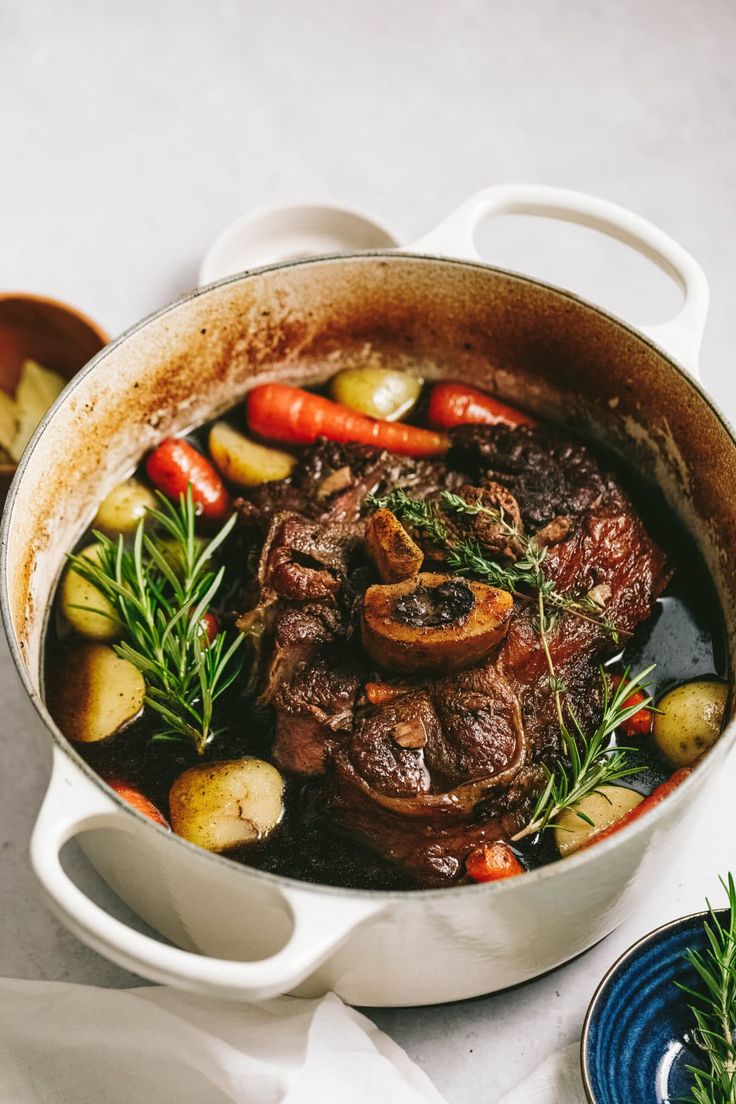 a pot filled with meat and vegetables on top of a white tablecloth next to two bowls