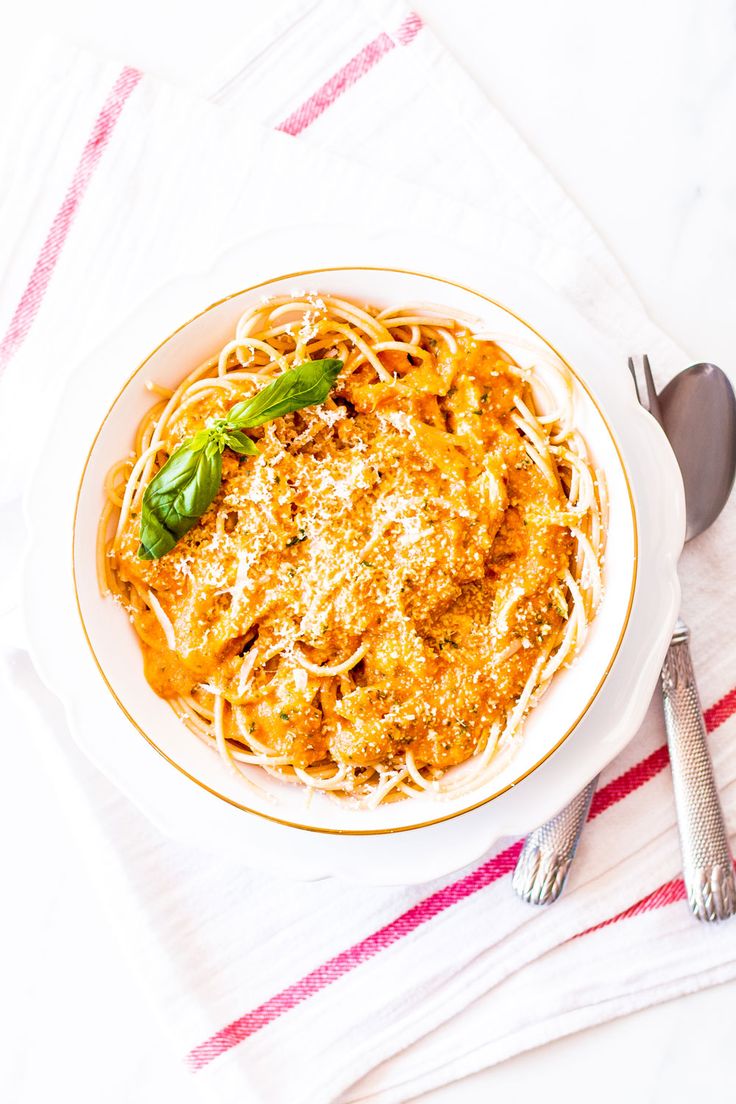 a white bowl filled with pasta on top of a table next to utensils