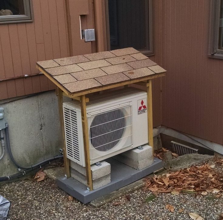 a small air conditioner sitting in front of a house with a shingled roof